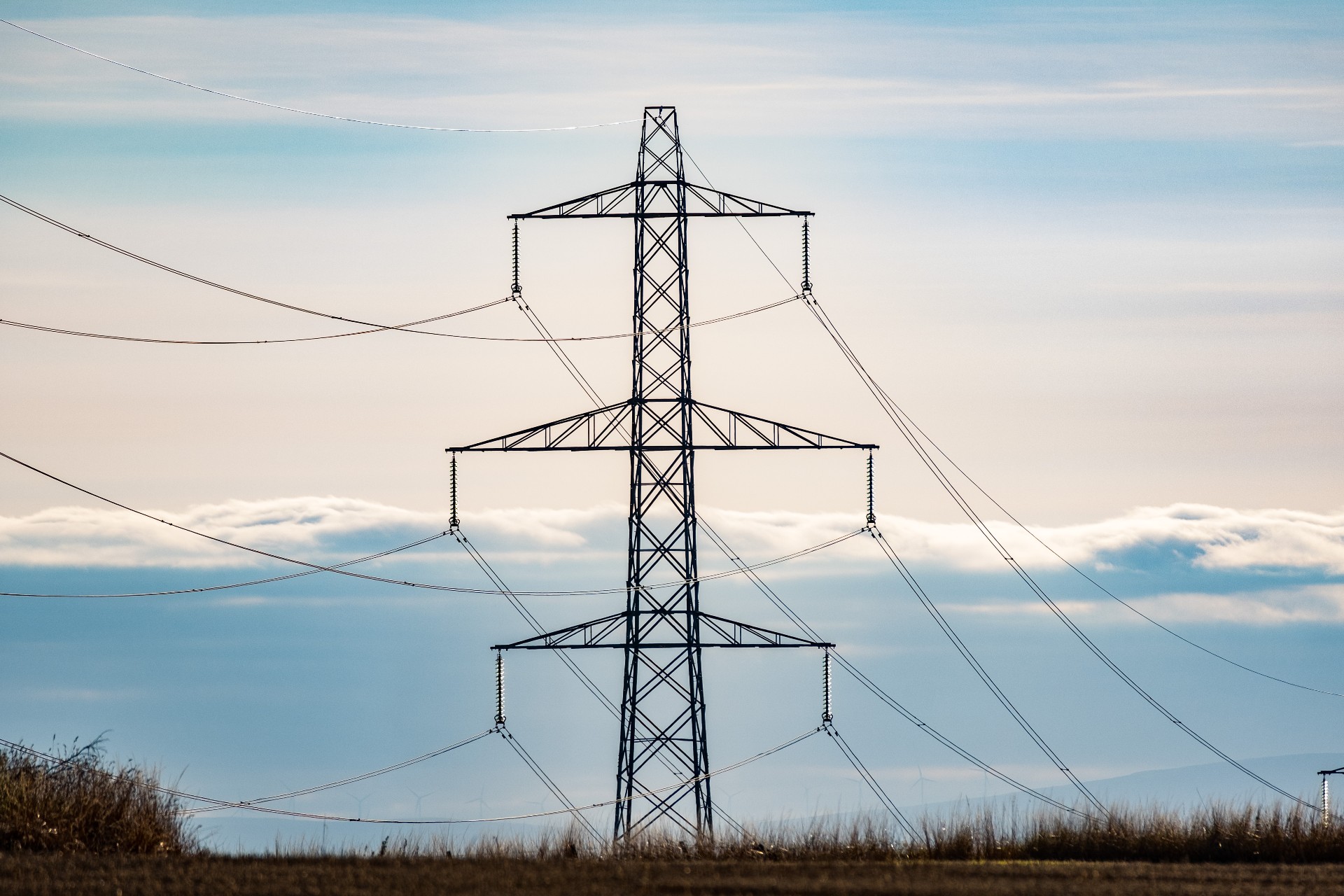 An electricity transmission pylon/tower in front of a pale blue sky filled with clouds