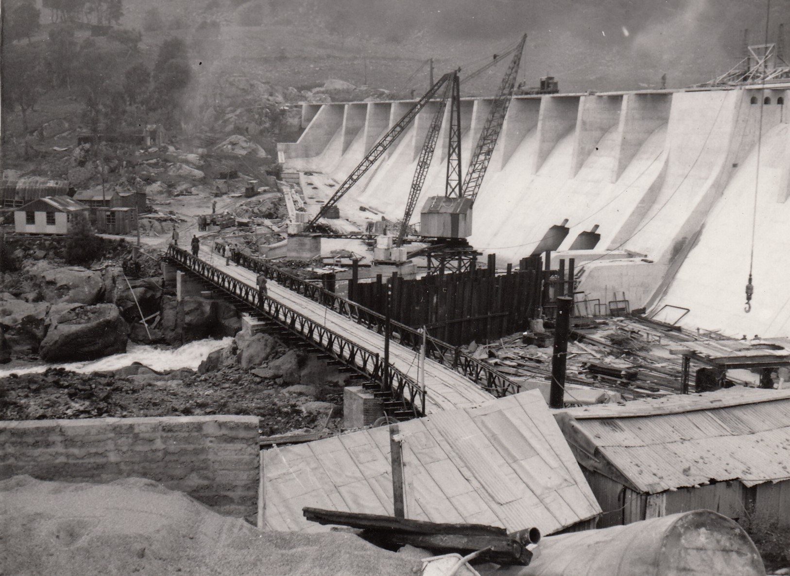 A black and white photo that is historical depicting the building of a hydro electric dam with cranes and exacvations shown 