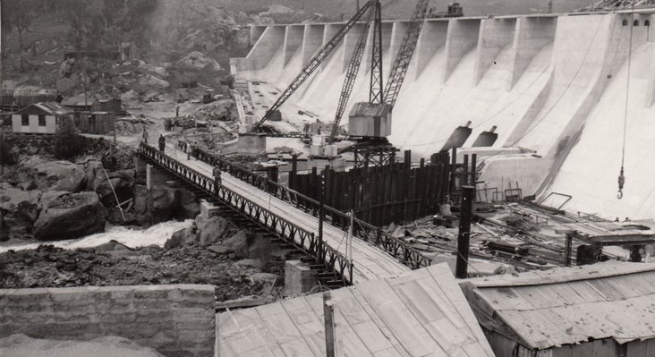 A black and white photo that is historical depicting the building of a hydro electric dam with cranes and exacvations shown 
